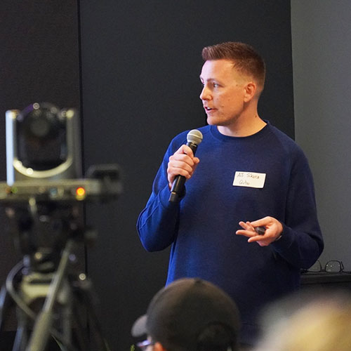 a man at a conference holds a mic and looks at something to the left, out of frame