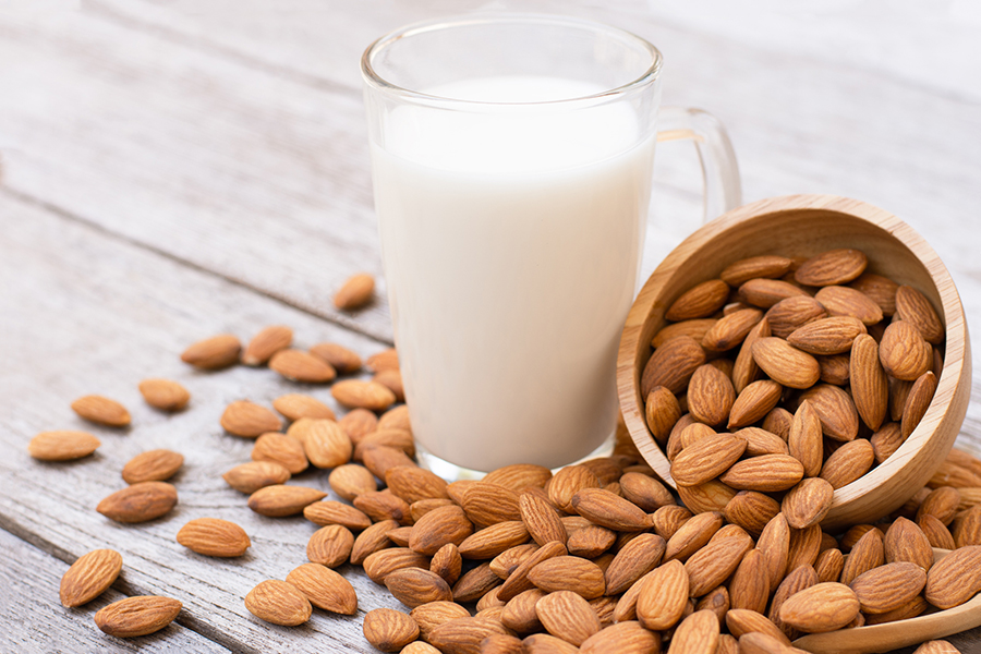 almond milk in a glass beside a dish and pile of almonds