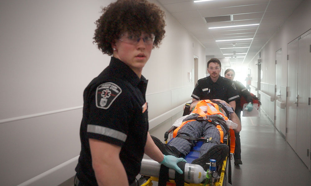 paramedic students move an actor patient on a stretcher down a hallway