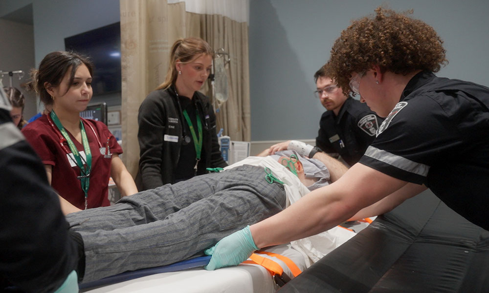 health care students around a patient in a bed in a simulated hospital room