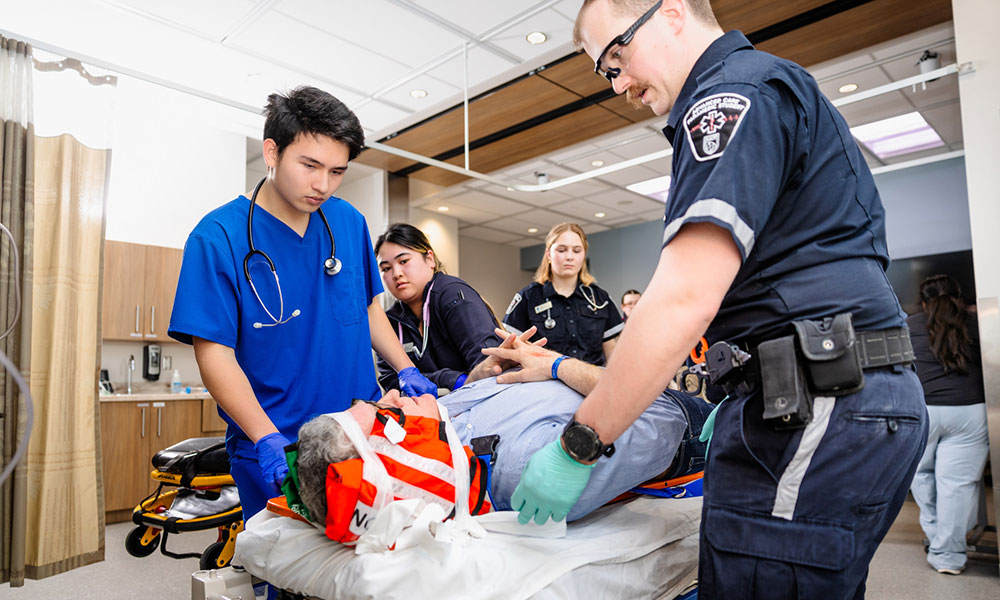 a group of health-care students treat an actor-patient lying in a bed in a hospital room