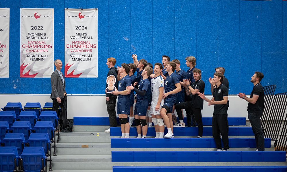 A group of athletes unveil a large championship banner inside a sports facility.
