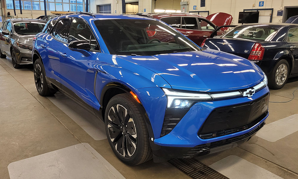Svijetloplavi Chevrolet SUV parkiran je unutra među ostalim vozilima u automobilskoj radionici.