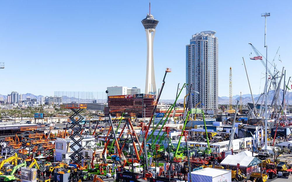 Wide view of a bustling outdoor construction expo filled with cranes and heavy equipment against the Las Vegas skyline.