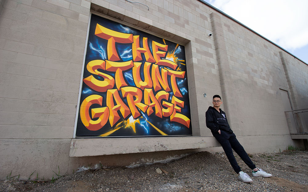 nait grad darron ta outside of the stunt garage, sitting in front of garage door painted with the gym name painted like graffiti