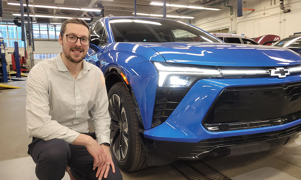 Osoba kleči pokraj svijetloplavog Chevrolet SUV-a u automobilskoj radionici.