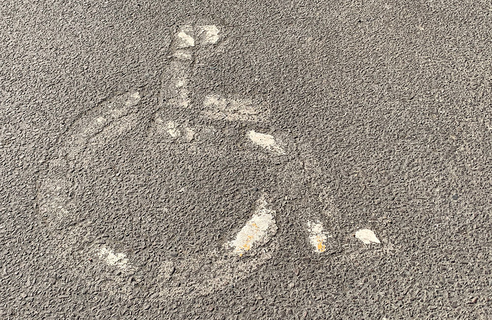 Faded wheelchair symbol painted on asphalt, indicating a worn-out accessible parking space.