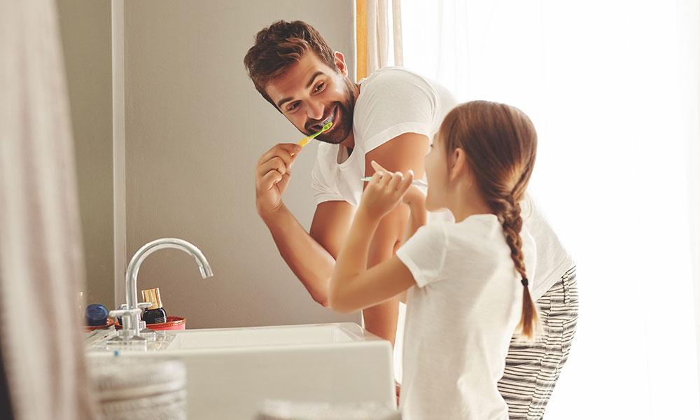 Adult and a child brushing their teeth together at a bathroom sink.