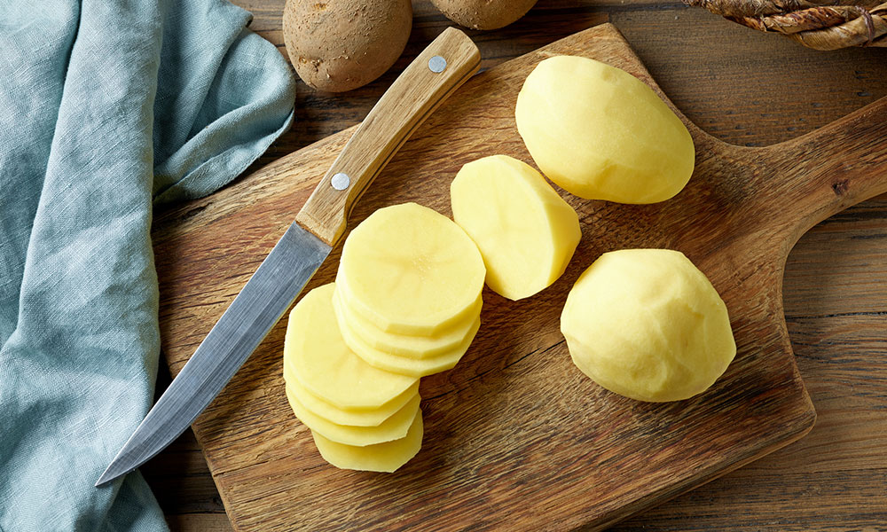 fresh cut potatoes on wooden board with knife