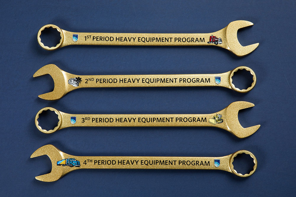 four golden wrenches lined up on a blue background. each wrench is marked with words 1st, 2nd, 3rd or 4th period heavy equipment program