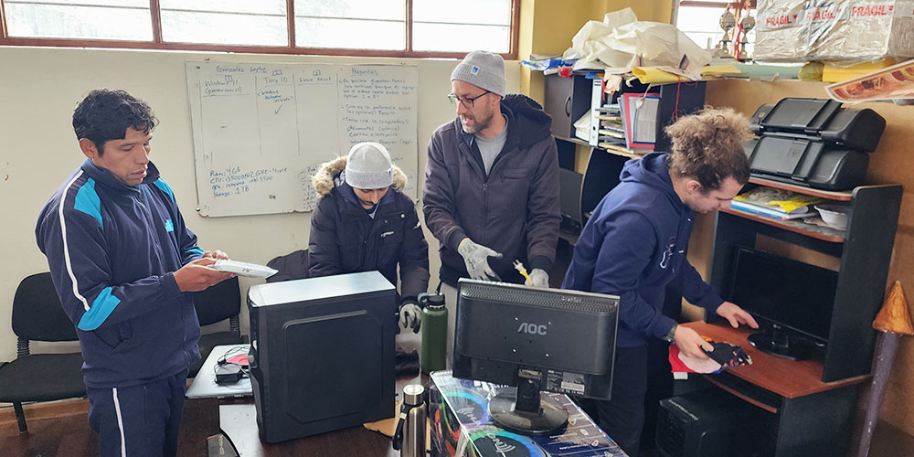 several people in jackets and warm hats work to assemble computers in a classroom