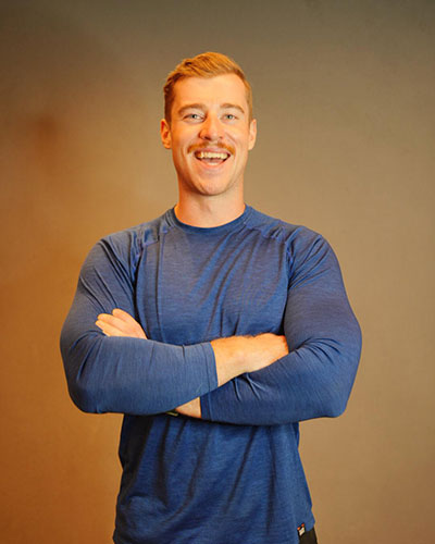 Person standing with arms crossed, wearing a fitted long‑sleeve blue athletic shirt against a plain background.
