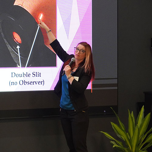 woman holding a mic and pointing to an image on a screen that appears to be part of a telescope