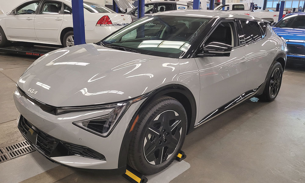 Srebrna Kia EV6 parkirana je u auto radionici među ostalim servisnim prostorima i vozilima.