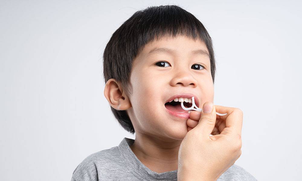 Child’s teeth being flossed with a floss pick.