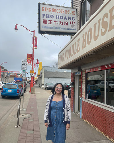 A woman stands on a street in front of a vietnamese pho restaurant