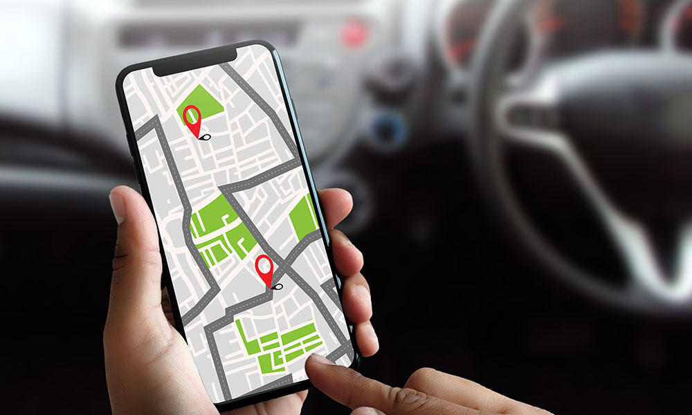 A hand holding a smartphone showing a navigation map with location pins inside a car.