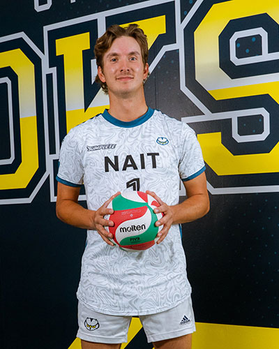 An athlete in a NAIT volleyball uniform holds a Molten volleyball in front of a large Ooks-themed backdrop.