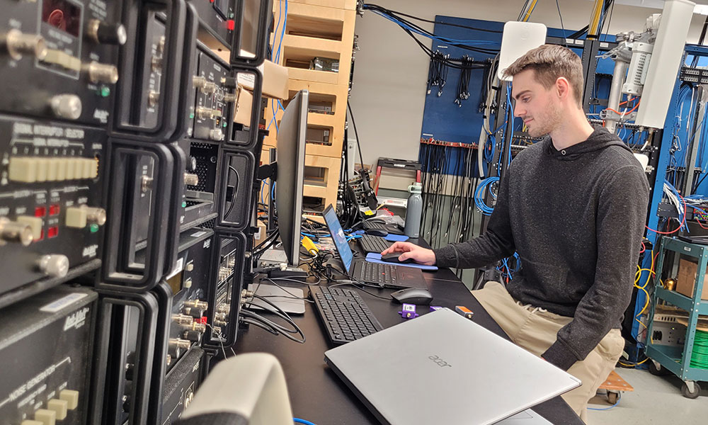 photo of nait wireless systems engineering student matthew nelson sits at a laptop amidst radio equipment
