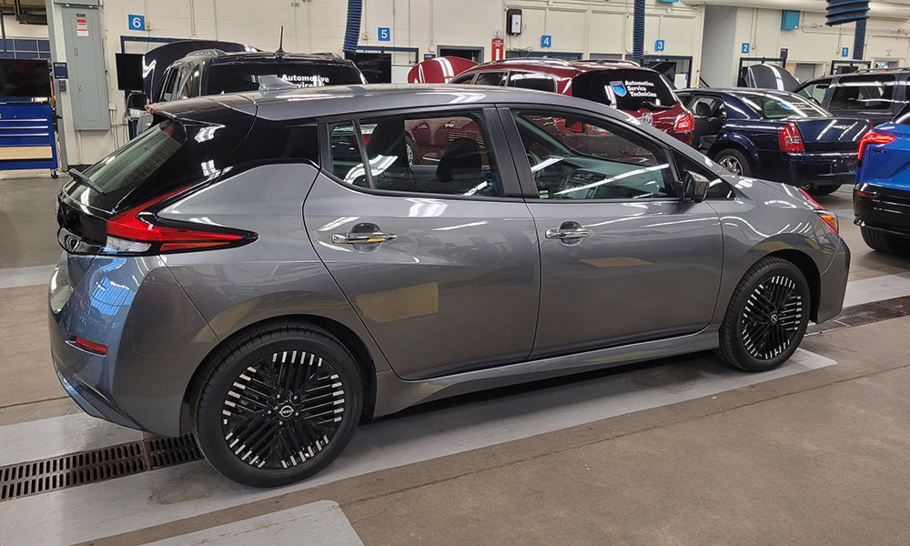 Sivi Nissan Leaf parkiran je u automobilskoj radionici među ostalim vozilima i servisnim prostorima.