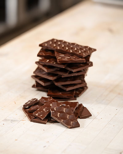 Stack of dark chocolate bars and pieces arranged on a wooden work surface.