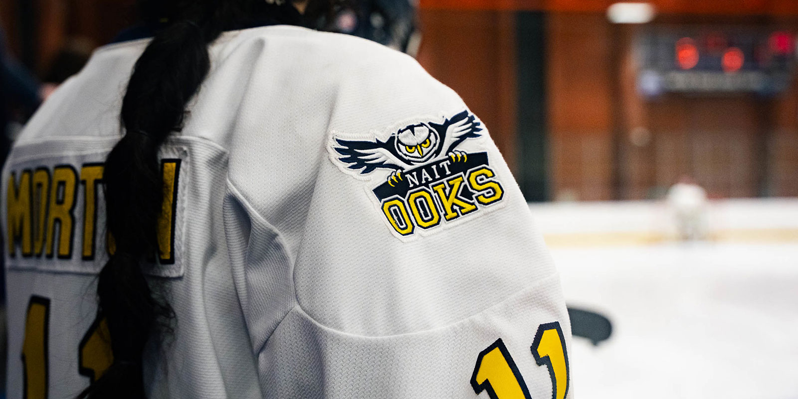 Close-up of a white hockey jersey showing the NAIT Ooks logo on the shoulder. The name “Morton” and number “11” are partially visible on the back.