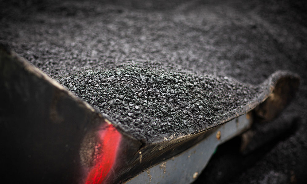 a close up of a large metal hopper full of granular black pieces of asphalt about to be laid as a road