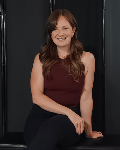Person seated against a dark backdrop wearing a sleeveless athletic top and leggings, posed in a relaxed posture.