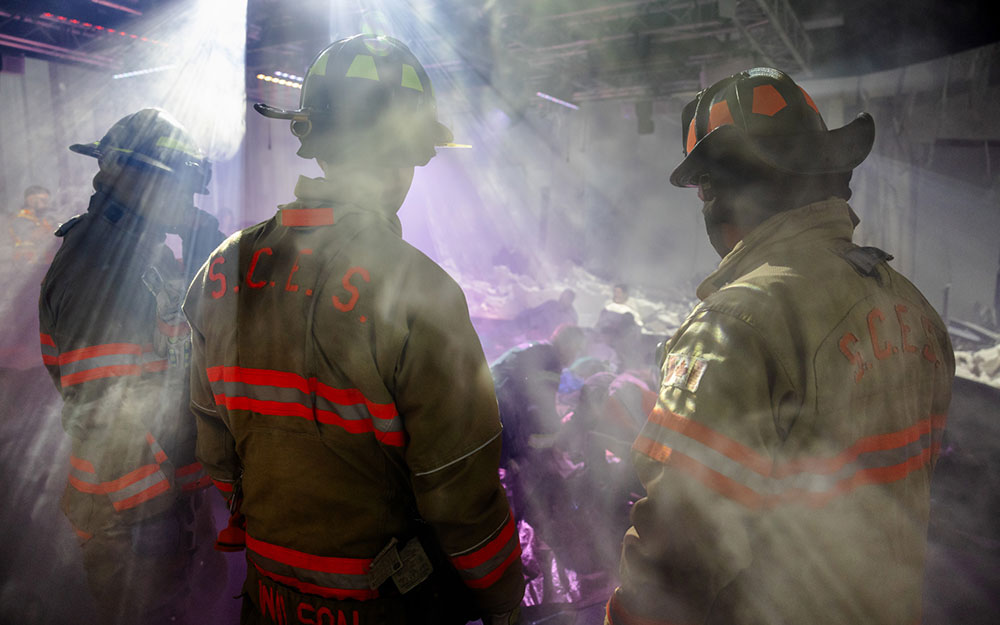 Firefighters in full turnout gear stand in a smoke-filled simulation environment during an emergency training exercise.