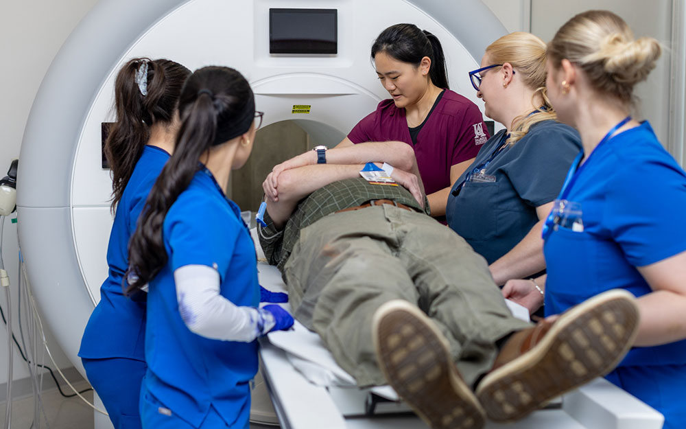 Healthcare students position a patient on an MRI scanner table during a hands-on medical imaging training session.