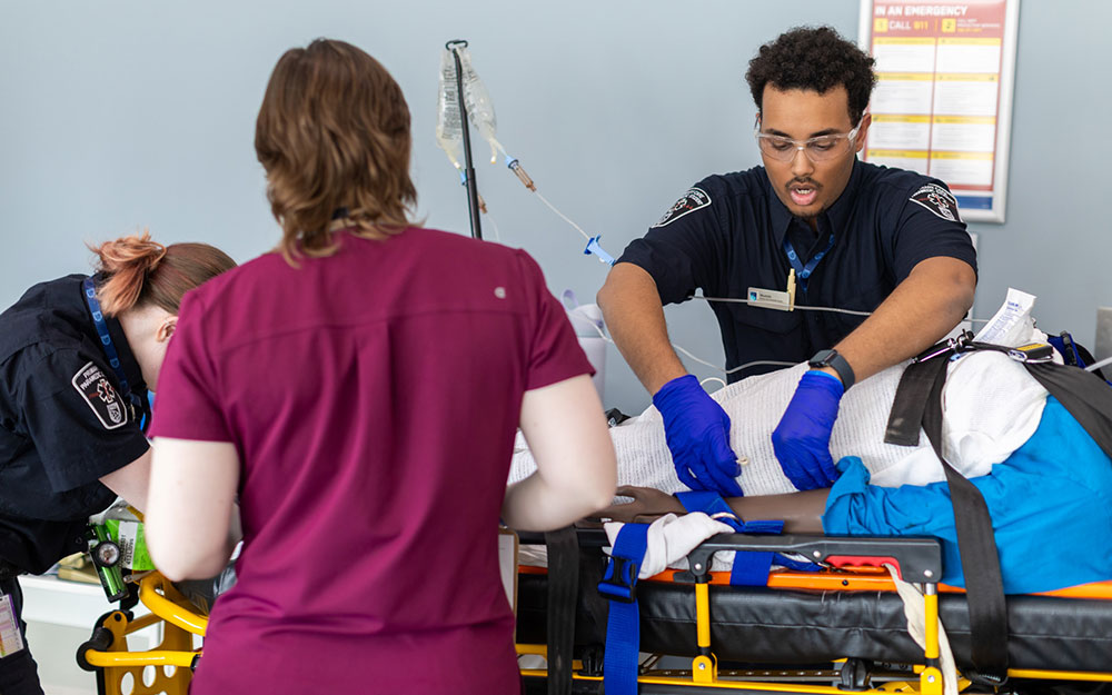 Emergency responders provide hands-on medical treatment to a patient secured on a stretcher during a simulation exercise.