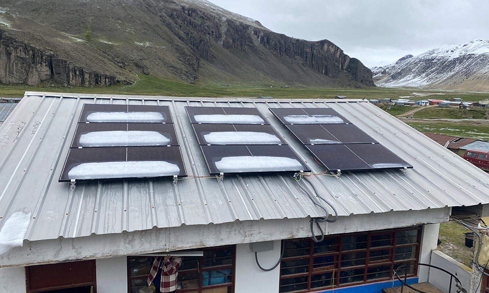 Solar panels covered in snow on a corrugated metal roof, with mountains and a village in the background.