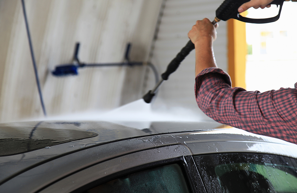 man spraying the top of a vehicle at the car wash