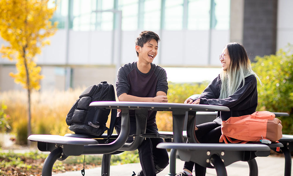 male and female student sitting at table in quad talking and laughing
