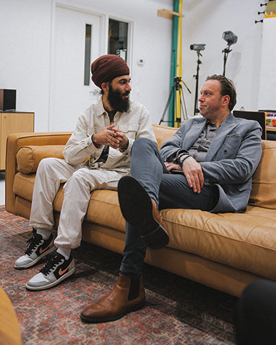 two men in suits sitting on a tan leather couch and having a conversation