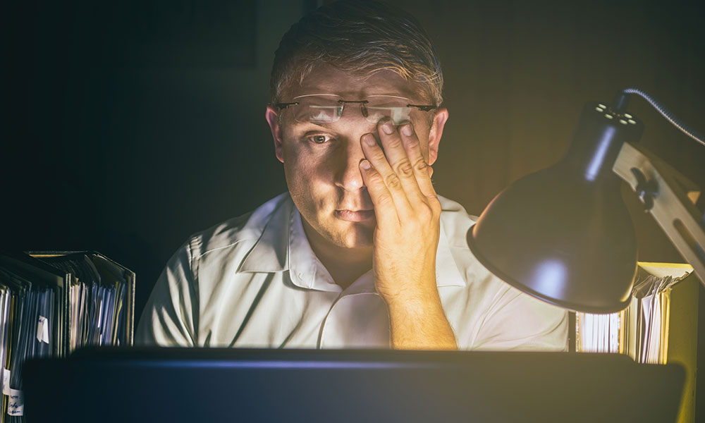 tired man sitting in front of computer at night