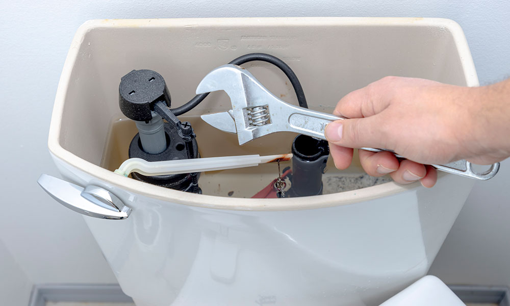 someone holding a wrench over an open toilet tank for repair