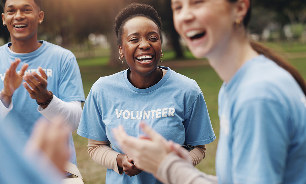 three women in light blue shirts with the word Volunteer on them laugh together
