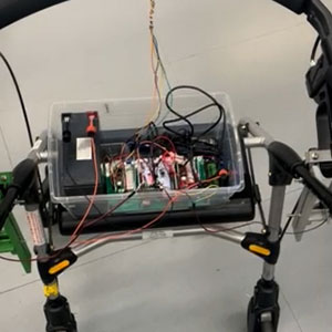 Alt text: Top view of a walker with a clear plastic box mounted on its frame, containing circuit boards and wiring for an electronic modification project.