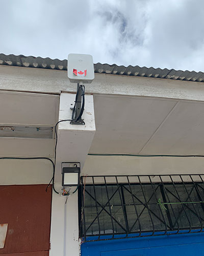 A white box-like internet transceiver with a Canadian flag sticker mounted on a building's exterior wall, with wires running along the wall.