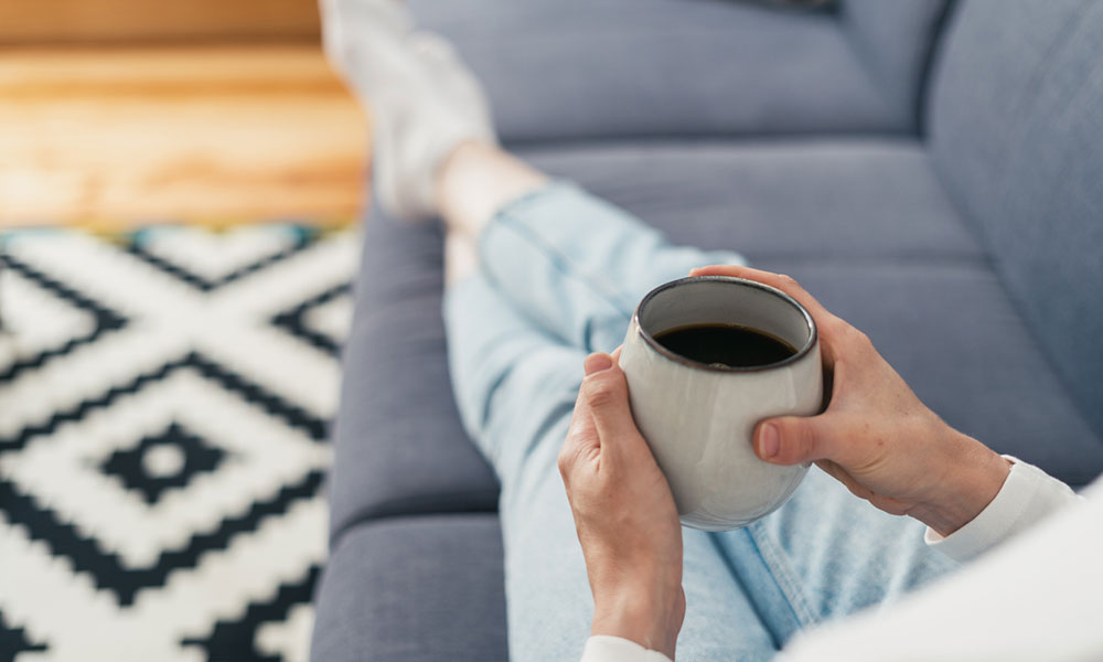 woman sitting on couch with feet up drinking coffee