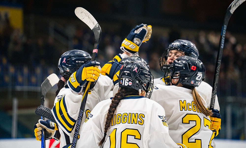 Hockey players in white jerseys with yellow and blue accents raising their sticks in celebration on the ice.