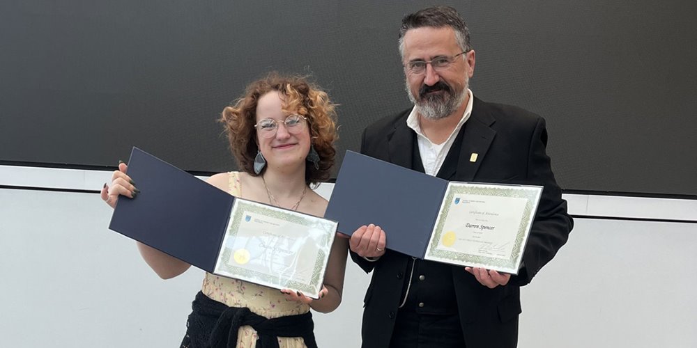 two people stand side by side and hold open post-secondary diploma parchments as they pose for a photo