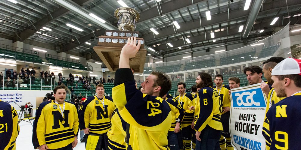men's hockey team celebrates a championship win after a game. they wear yellow jerseys with large blue Ns on the front. one player holds a trophy above his head.