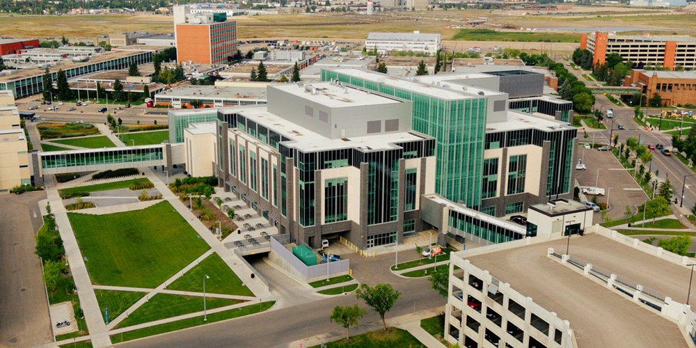 aerial shot of nait main campus with a large modern building made of stone and glass in the foreground, as well as a green space