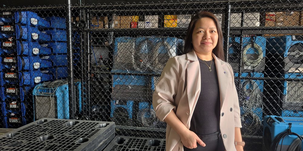a woman in a pale jacket and dark shirt poses for a photo in a tidy warehouse