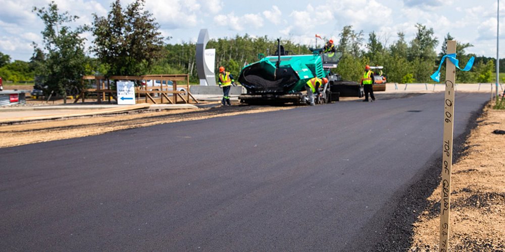 a stretch of newly laid asphalt leading to construction worker in the distance