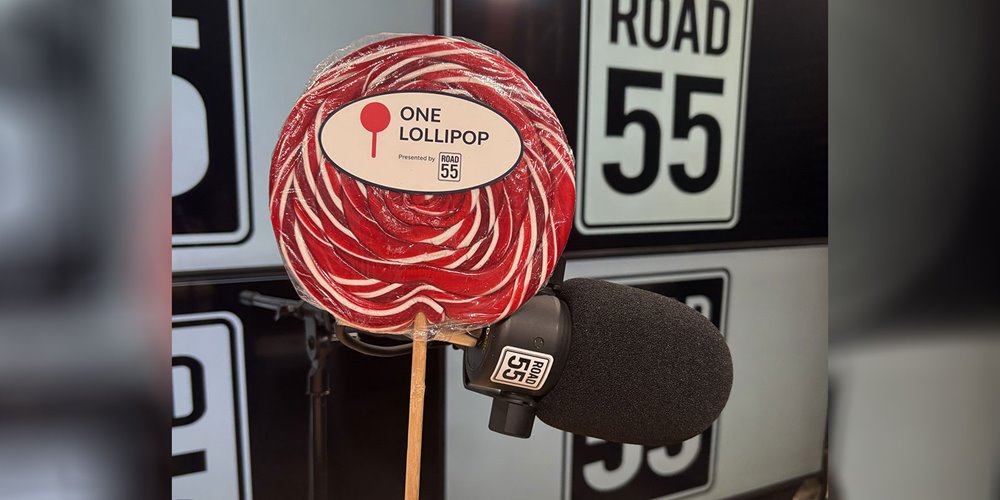 Red-and-white swirl lollipop on a stick positioned in front of a microphone with Road 55 signage in the background.