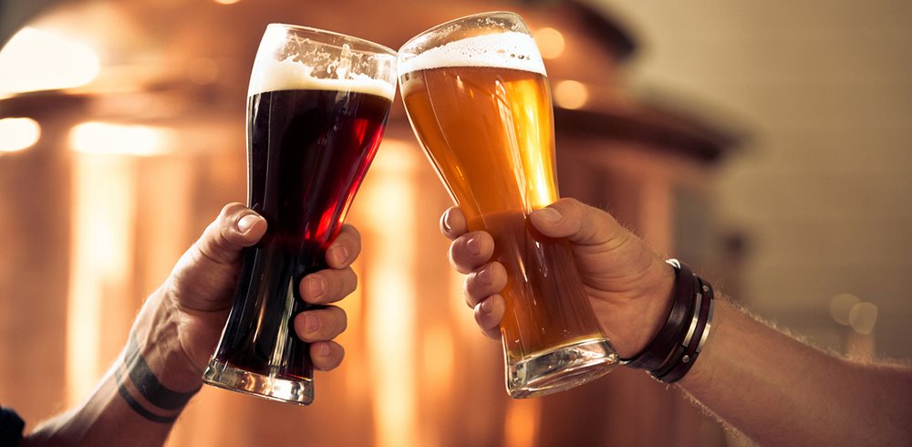 people clinking beer glasses together; one is dark the other is light