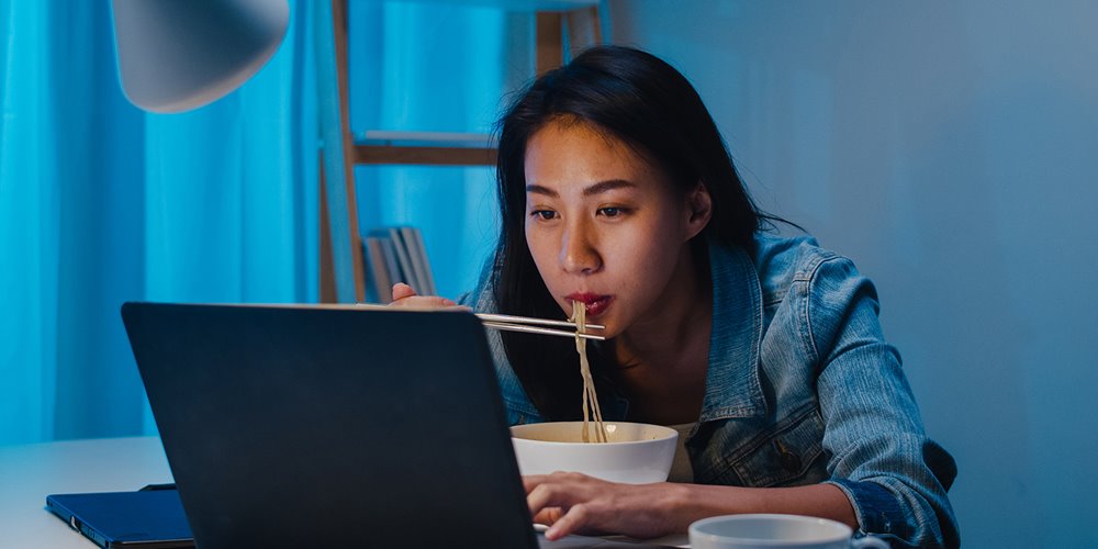 girl eating noodles while looking at laptop